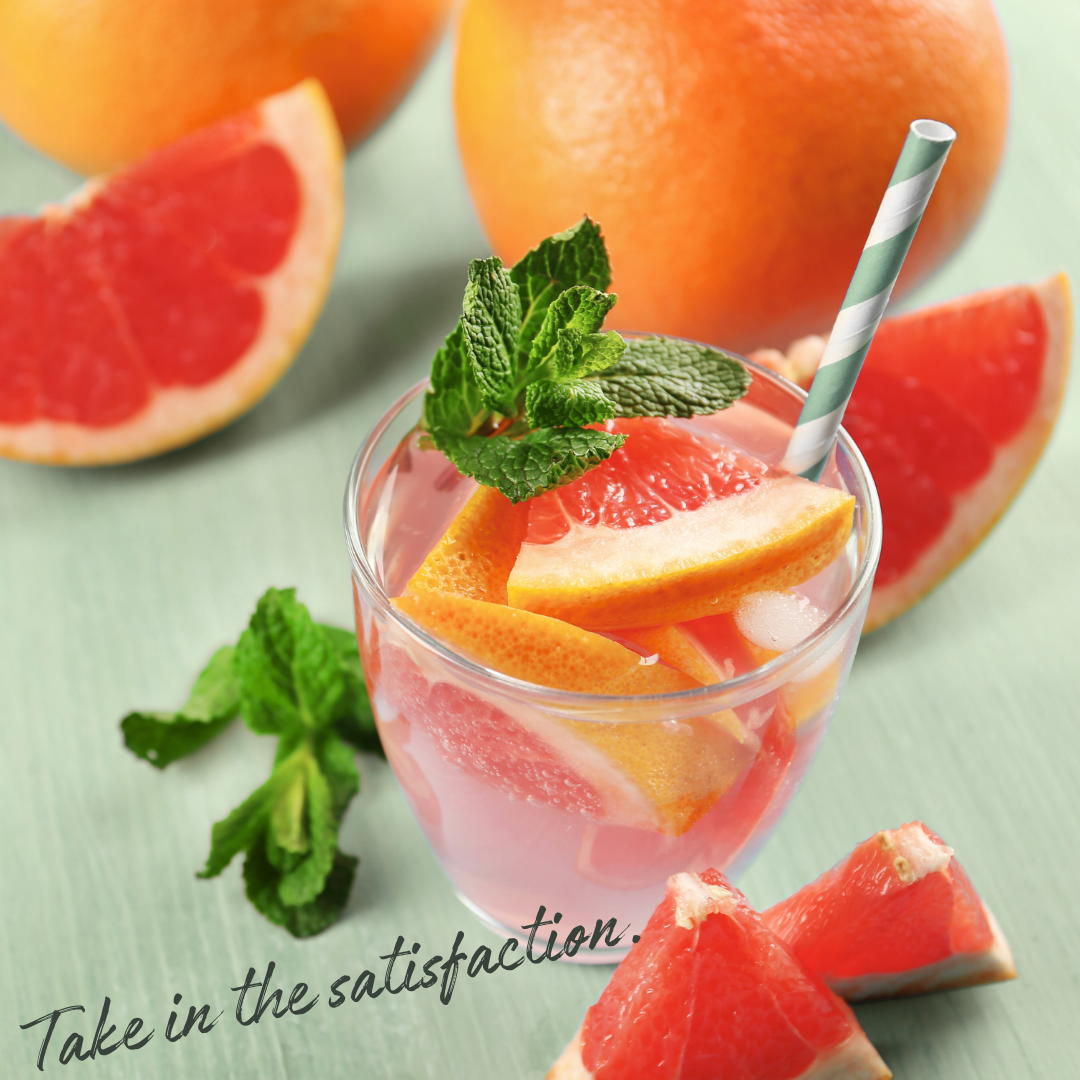 Glass of grapefruit juice with slices and mint leaves, surrounded by whole and sliced grapefruits on a light green background.